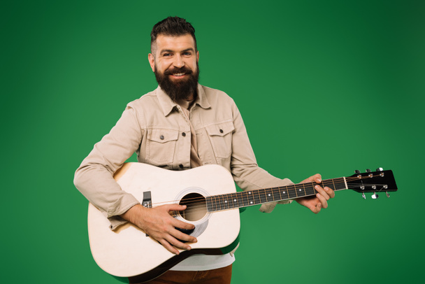 cheerful handsome man playing on acoustic guitar, isolated on green - Foto, Imagem
