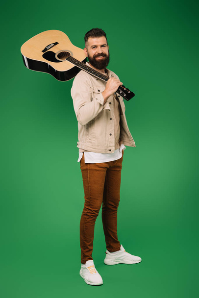 handsome guitarist holding acoustic guitar, isolated on green - Photo, Image