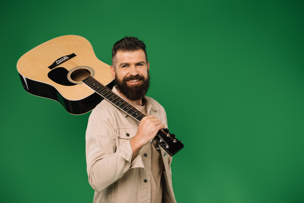handsome smiling man holding acoustic guitar, isolated on green - Fotoğraf, Görsel