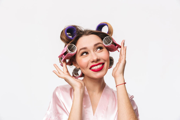 Beautiful housewife with curlers in hair standing isolated over white background, posing - Photo, Image