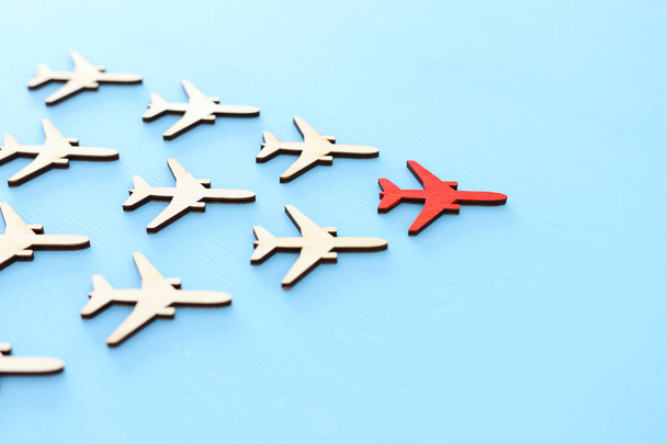 Leadership concept with airplanes on blue wooden background. One red leader flays ahead others. - Photo, image