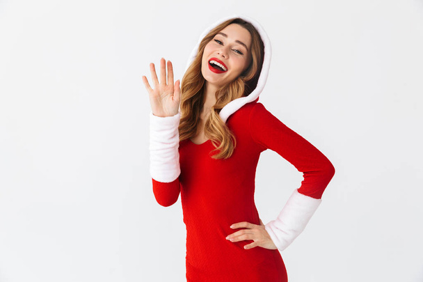Изображение очаровательной женщины 20 лет в рождественском красном платье, размахивающей рукой на белом фоне
 - Фото, изображение