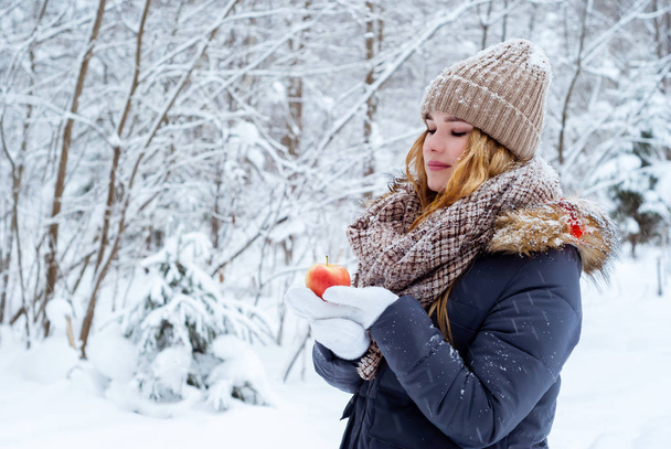 menina calorosamente vestida no fundo de uma paisagem de inverno olha atentamente para uma maçã em sua mão
 - Foto, Imagem