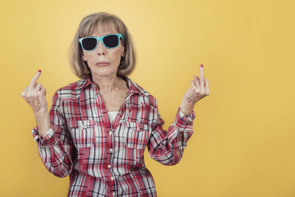 Portrait of senior woman with sunglasses insulting with finger - Photo, Image