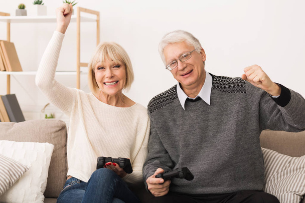 Elderly couple playing video games, celebrating victory - Foto, afbeelding
