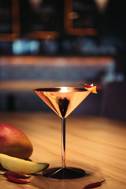 alcoholic cocktail in metal glass decorated with chili pepper, nacho chip and mango on wooden table - 写真・画像