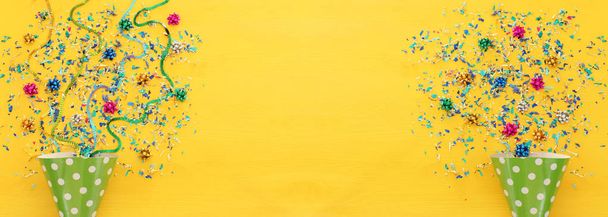 Party colorful confetti and clown hat over yellow wooden background . Top view, flat lay - Foto, Imagen