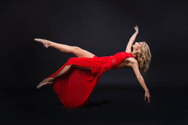 beautiful young girl with hairstyle and make-up in a red dress in flight on a black background - Foto, Imagen