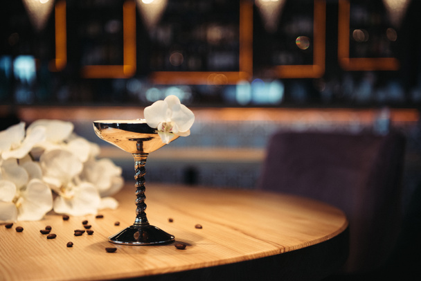 koktajl alkoholowy w metal szkło zdobione orchidei i ziarna kawy na drewnianym stole - Zdjęcie, obraz