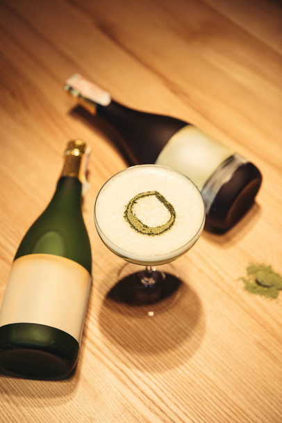 delicious cocktail with foam on wooden table with bottles of champagne on background - Fotografie, Obrázek