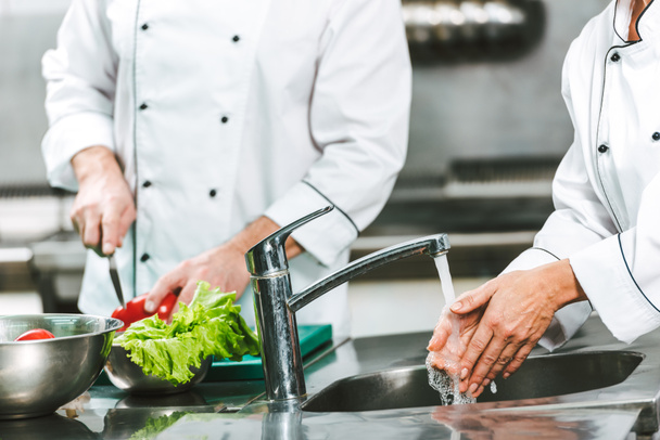 cropped view of female chef washing hands over sink while colleague cooking on background in restaurant kitchen - Photo, Image