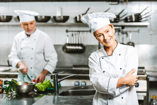 bela cozinheira e chef masculino em casacos de peito duplo durante a culinária na cozinha do restaurante
  - Foto, Imagem