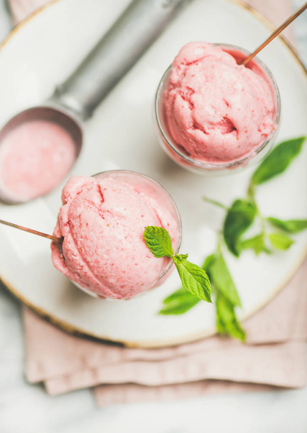 Healthy low calorie summer dessert. Homemade strawberry yogurt ice cream with fresh mint in glasses on plate over grey marble table background, top view, close-up. Clean eating, dieting food concept - Photo, Image