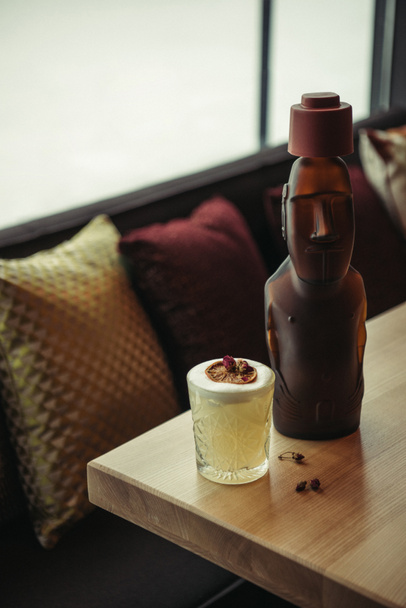 бронзовая статуя и алкогольный коктейль украшены сухим апельсином на деревянном столе в ресторане
 - Фото, изображение