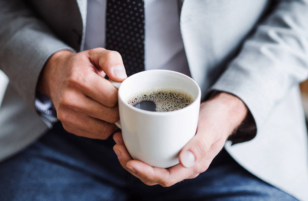 A midsection of businessman sitting in an office, holding a cup of coffee. - Foto, immagini