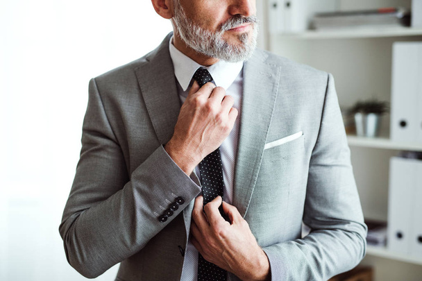 Мидсекция зрелого бизнесмена, стоящего в офисе, держащего галстук
. - Фото, изображение