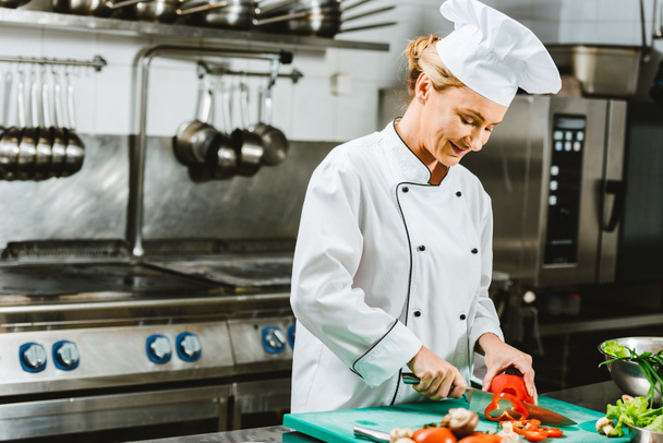 beautiful female chef in uniform cutting pepper in restaurant kitchen - 写真・画像