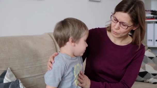 Cute little boy is coughing, sitting with his mother in a living room - Materiał filmowy, wideo