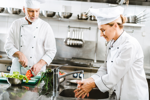 selective focus of male and female chefs in double-breasted jackets cooking in restaurant kitchen - Foto, Bild