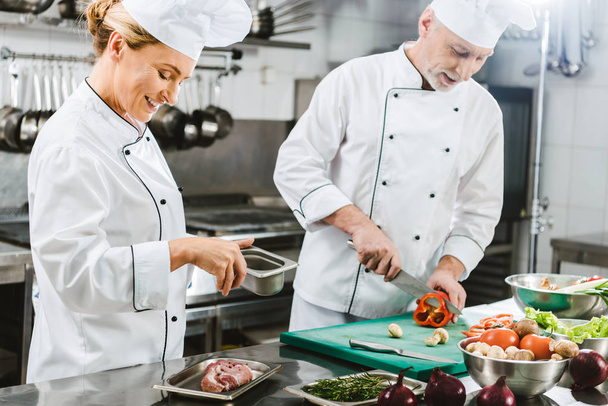 chefs masculinos y femeninos en uniforme preparando comida en la cocina del restaurante
 - Foto, imagen
