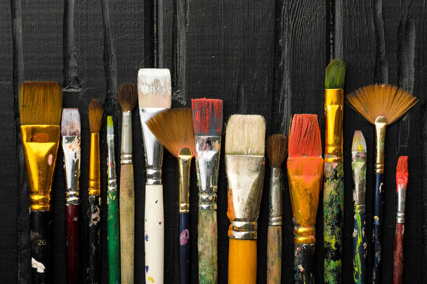 Καλλιτέχνες εργαλεία, βούρτσες στη ζωγραφική είναι σε μια σειρά πάνω σε μαύρο φόντο ξύλινη. - Φωτογραφία, εικόνα