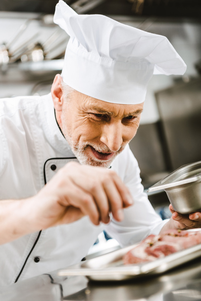 male chef in uniform seasoning dish in restaurant kitchen - Foto, Imagen