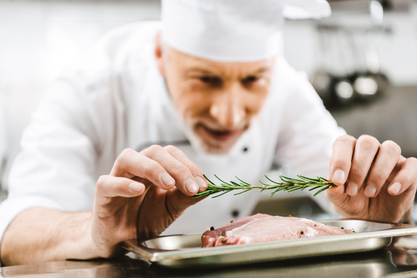 férfi szakács egységes díszítő hús étel, rozmaring gyógynövény-restaurant konyhában - Fotó, kép