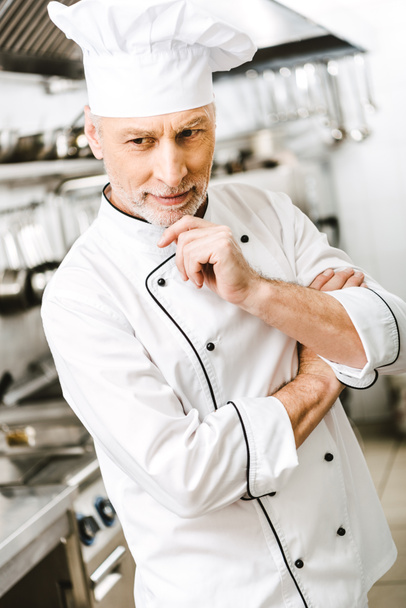 selective focus of handsome pensive male chef propping chin with hand in restaurant kitchen - Фото, изображение