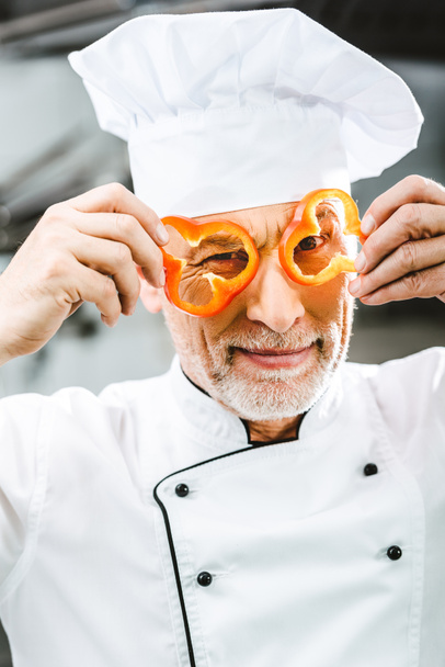 chef maschio in uniforme e cappello con fette di pepe davanti al viso nella cucina del ristorante
 - Foto, immagini
