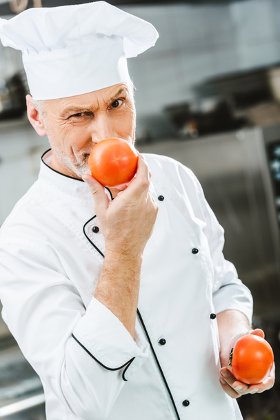 male chef in uniform and hat holding tomatoes in restaurant kitchen - Foto, imagen