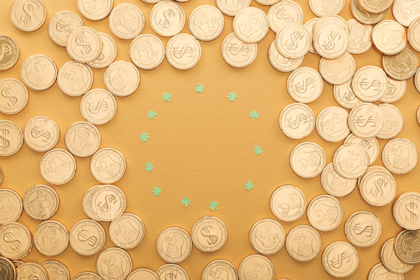 Top uitzicht op gouden munten met dollartekens en cirkel van shamrocks geïsoleerd op oranje, st patrick dag concept - Foto, afbeelding