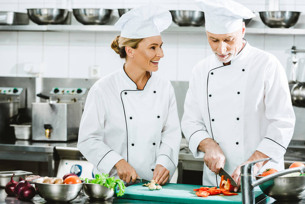 female and male chefs in uniform cutting ingredients while cooking in restaurant kitchen - Photo, image