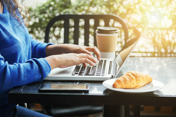 Nelze rozpoznat žena sedí u stolu venkovní kavárna poblíž croissant a šálek horkého nápoje a procházení moderní laptop - Fotografie, Obrázek