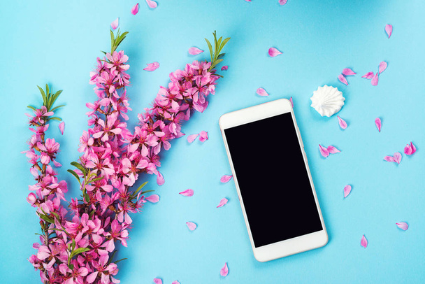 Flatlay met smartphone mock up en bloemen. Bloemmotief op blauwe achtergrond. Bovenaanzicht. Samenstelling van de bloemen. Lente achtergrond met mobiele telefoon.  - Foto, afbeelding