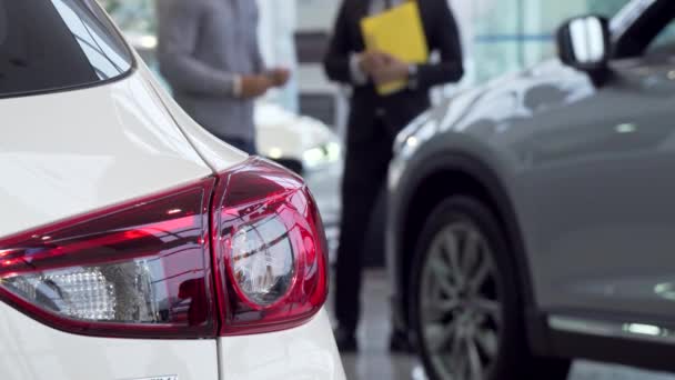 Selectieve aandacht op een auto, verkoper in gesprek met de klant op de achtergrond - Video