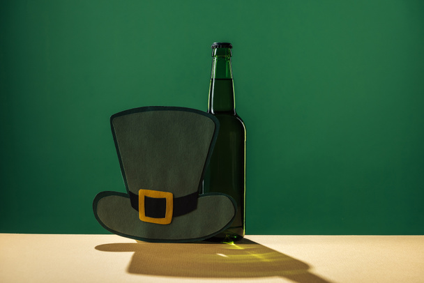 бутылки пива и бумажная шляпа изолированы на зеленый, День святого Патрика концепции
 - Фото, изображение