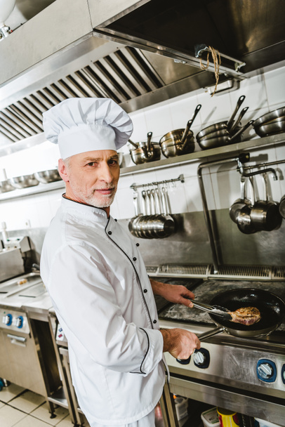 шеф-повар в униформе, готовит мясо на кухне ресторана
 - Фото, изображение