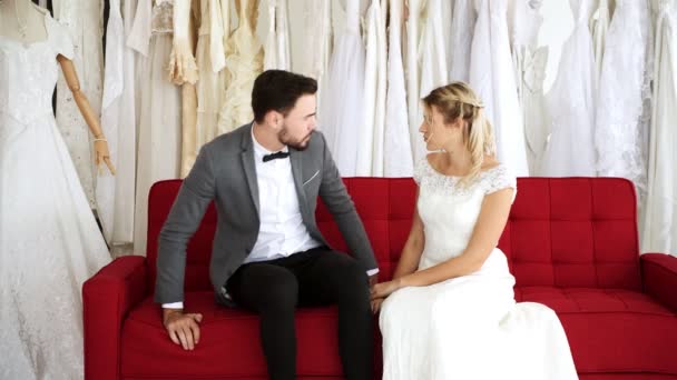 Romantic wedding couple in expensive dress shop. White man and woman in bride dress, woman gently wake his man up in sofa. Romantic young couple concept. - Imágenes, Vídeo