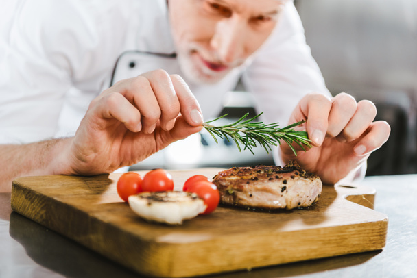 close up of male chef in uniform decorating meat steak with rosemary in restaurant kitchen - 写真・画像
