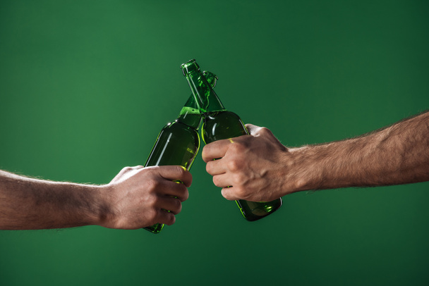 partial view of men clinking beer bottles isolated on green, st patrick day concept - Foto, Imagem