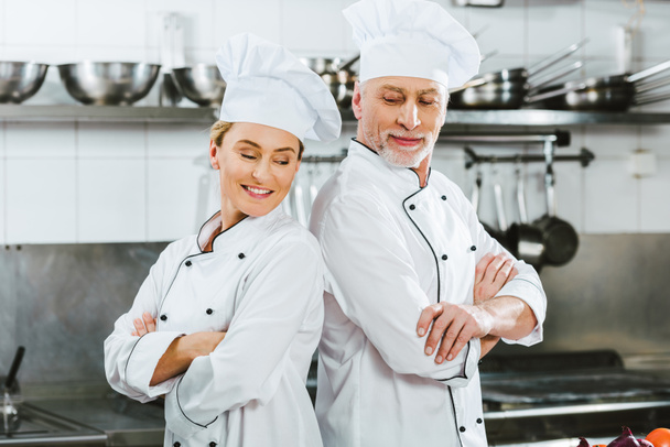 smiling chefs in uniform with arms crossed at restaurant kitchen - Фото, зображення
