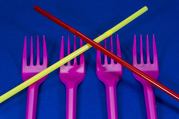 Розовые столовые приборы пластиковые вилки и соломинки расположены на синем фоне. Концепция проблемы пластиковых отходов
 - Фото, изображение