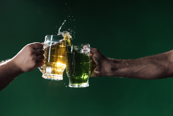przycięte widzenia mężczyzn sakiewkach brzęczały szklanki piwa z plamami na białym tle na ciemno zielony, st patrick dzień koncepcji - Zdjęcie, obraz