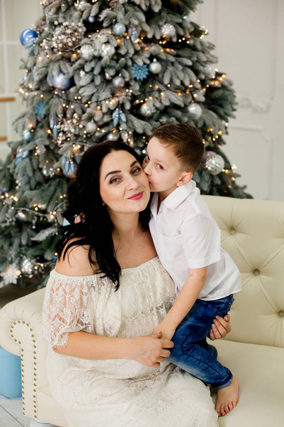 mooie moeder met zoon op de Bank in de buurt van de kerstboom - Foto, afbeelding
