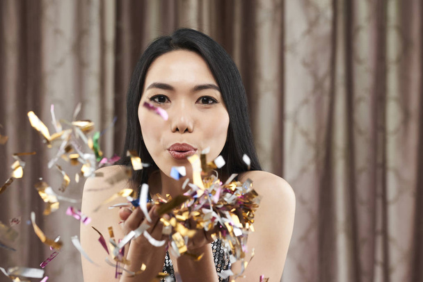 Hermosa joven vietnamita mujer soplando confeti chispeante
 - Foto, Imagen
