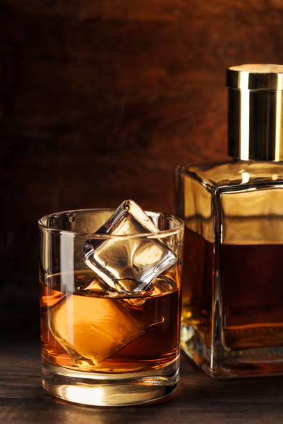 vista de cerca del vaso de whisky con cubitos de hielo y botella en la mesa de madera
  - Foto, Imagen