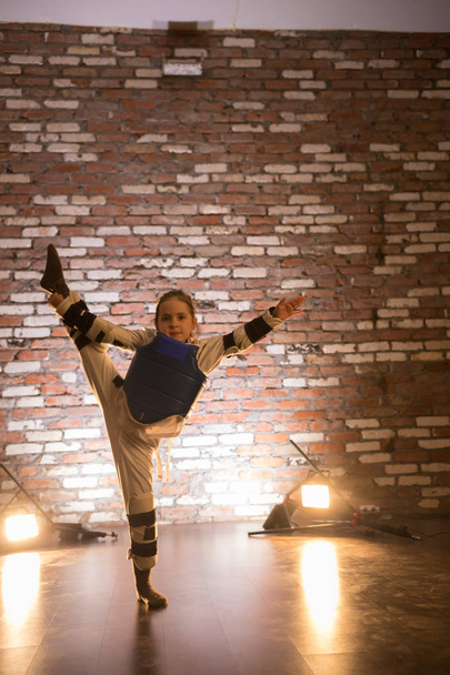 Karate edzéseket sárga fény a stúdióban. Egy kislány mutatja, ő nyújtás - Fotó, kép