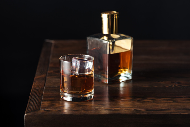 glass and bottle of whisky on dark wooden table isolated on black   - Фото, изображение
