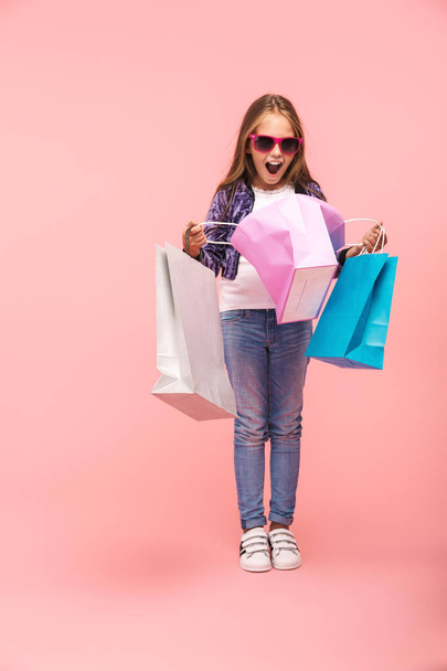 Cheerful little girl isolated over pink background, carrying shopping bags - Fotografie, Obrázek