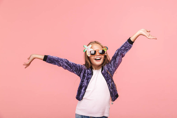 Portrait of a cheerful little girl wearing summer sunglasses standing isolated over pink background - Фото, зображення
